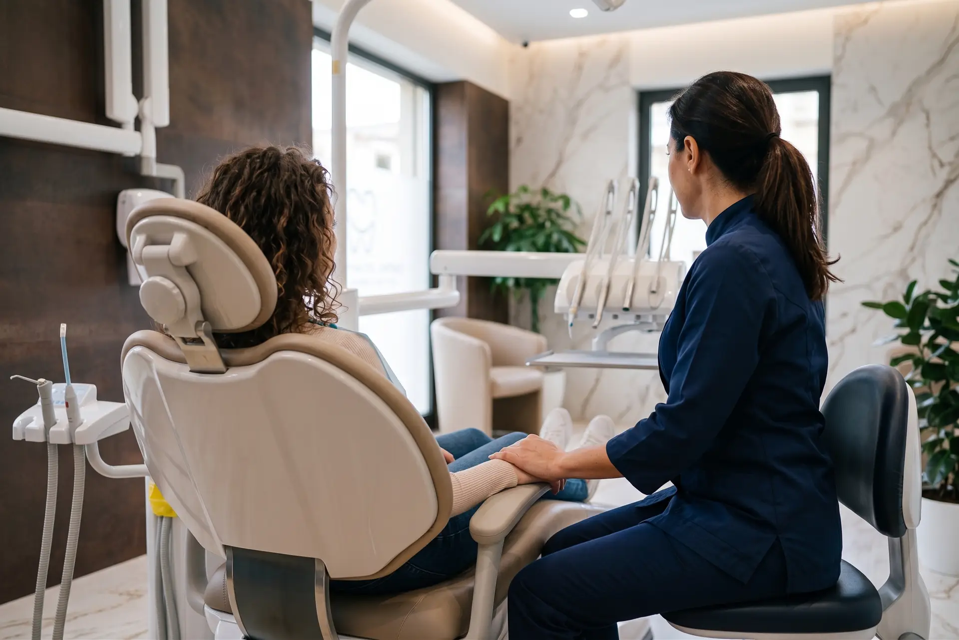 Primo piano delle mani della Dott.ssa Mistretta che confortano una paziente seduta di spalle, all'interno del Centro Odontoiatrico Ambra Mistretta a Castelvetrano.